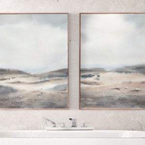 Peut inclure: Deux peintures &agrave; l'aquarelle encadr&eacute;es d'un paysage avec une palette de couleurs douces de gris, de bruns et de bleus. Les peintures sont accroch&eacute;es &agrave; un mur gris clair au-dessus d'une baignoire blanche.