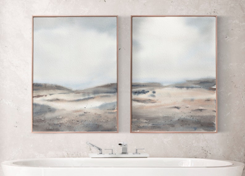 Peut inclure: Deux peintures &agrave; l'aquarelle encadr&eacute;es d'un paysage avec une palette de couleurs douces de gris, de bruns et de bleus. Les peintures sont accroch&eacute;es &agrave; un mur gris clair au-dessus d'une baignoire blanche.