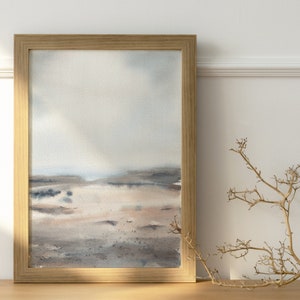 Peut inclure: Une peinture &agrave; l'aquarelle encadr&eacute;e d'un paysage avec un ciel bleu clair, une terre brune et grise et une touche d'eau au loin. La peinture est dans un cadre en bois brun clair.