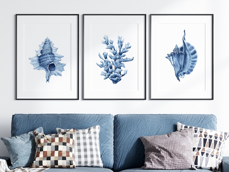 May include: Three framed prints with blue watercolor illustrations of seashells and coral. The prints are in black frames and are hung on a white wall.