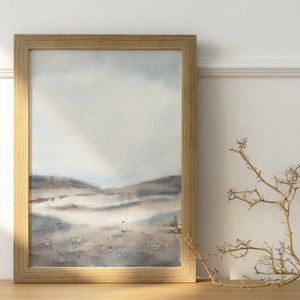 Peut inclure: Une peinture &agrave; l'aquarelle encadr&eacute;e d'un paysage avec un ciel bleu clair et des collines brunes. La peinture est dans un cadre en bois et est accroch&eacute;e &agrave; un mur blanc.