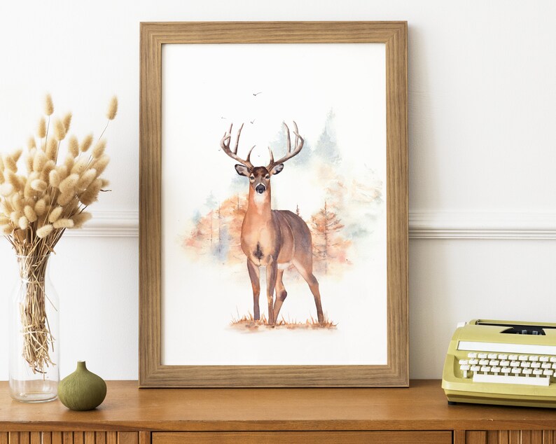 May include: A watercolor painting of a white-tailed deer standing in a forest. The deer is brown with a large rack of antlers. The background is a watercolor wash of brown, green, and blue.