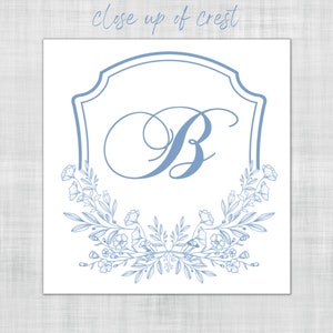 Op de afbeelding: Een lichtblauw wapenontwerp met de letter "B" in sierlijk schrift, omlijst door een decoratieve rand en bloemmotieven. De tekst "Close up of crest" staat bovenaan. Het ontwerp staat op een witte achtergrond.