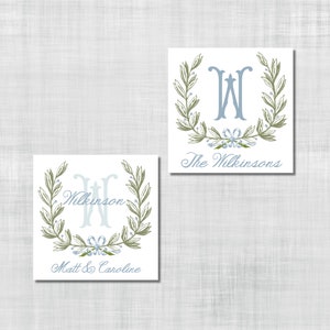 Op de afbeelding: Twee vierkante kaarten met een lichtblauw en groen ontwerp. Elke kaart heeft een grote letter "W" in lichtblauw, omringd door een groene olijftakkenkrans. Eén kaart leest "The Wilkinsons" en de andere "Matt & Caroline".