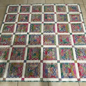 May include: A patchwork quilt with a white background and squares of various floral patterns in shades of pink, green, blue, and purple.