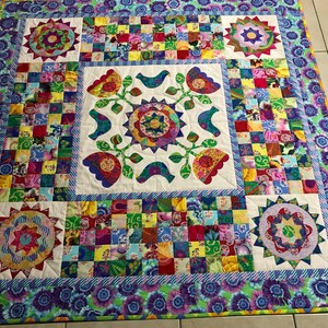 May include: A colourful patchwork quilt with a central design of stylised flowers and birds. The quilt is framed by a border of purple and blue flowers.