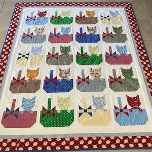 May include: A white quilt with a red, white and blue border. The quilt features a repeating pattern of cats in baskets. The cats are in various colours and patterns, including brown, blue, green and yellow.