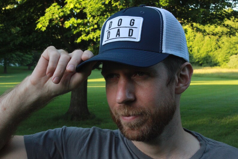 May include: A navy blue and white trucker hat with a white patch that says "DOG DAD" in black letters.