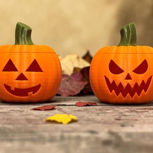 May include: Two orange plastic pumpkins with green stems and carved facial expressions. The left pumpkin features a simple triangular eye and nose design with a wide smile, while the right pumpkin displays sharp, jagged eyes and a toothy grin.