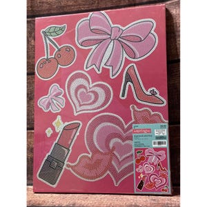 May include: A pink diamond painting kit featuring various designs including a large bow, a pair of cherries, a high-heeled shoe, hearts, lips, and a lipstick tube. The packaging includes the text "the spring shop" and "diamond painting".