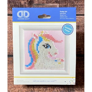 May include: A Diamond Dotz Pretty Uni diamond painting kit in a white frame. The packaging features a unicorn graphic with pink, blue, and yellow accents on a light pink background. The design size is 3.7 inches by 3.7 inches. Includes frame.