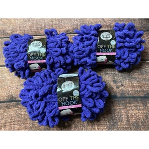 May include: Three skeins of deep purple Lion Brand Off The Hook Glitz yarn. Each skein features a black paper label with white text reading Off The Hook Glitz and a small logo. The yarn has a thick, looped texture with a subtle shimmering finish.
