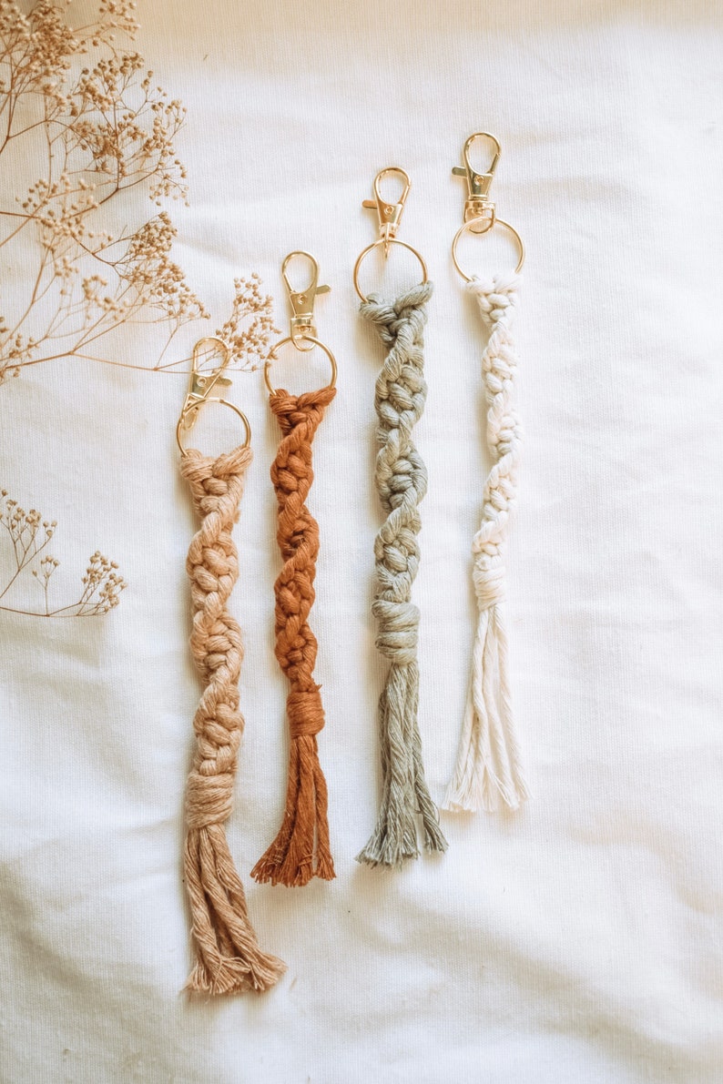 May include: Four handmade macrame keychains with gold key rings. The keychains are in shades of beige, brown, green, and white.