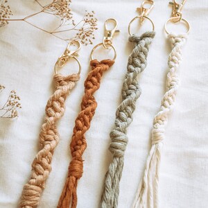 May include: Four handmade macrame keychains with gold metal key rings. The keychains are in shades of beige, brown, green, and white.