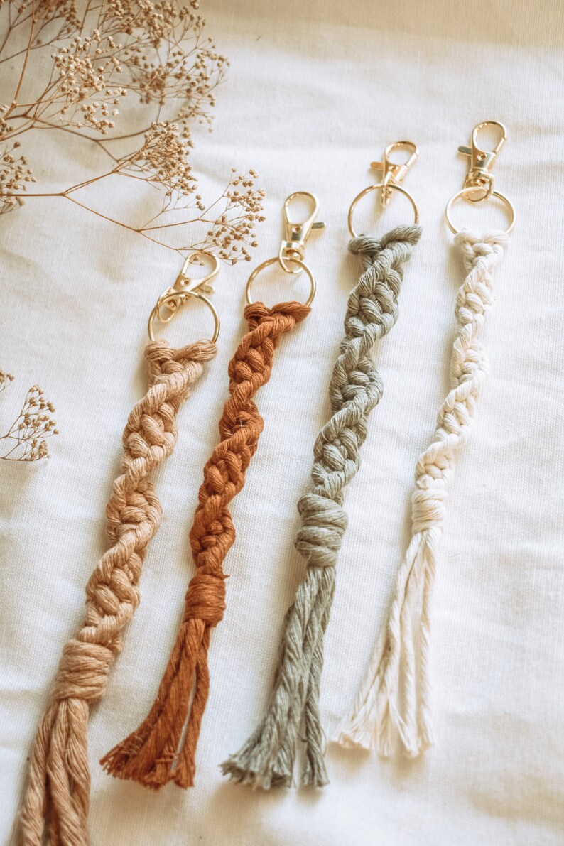 May include: Four handmade macrame keychains with gold metal key rings. The keychains are in shades of beige, brown, green, and white.