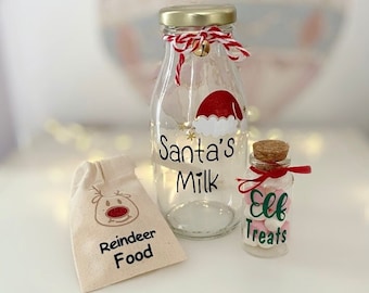 Puede incluir: Un conjunto de tres frascos de vidrio con decoraciones navideñas festivas. Los frascos están etiquetados como "Leche de Santa", "Golosinas de duendes" y "Comida para renos".