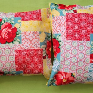 May include: Two decorative throw pillows with a patchwork design featuring red, yellow, and blue floral patterns. The pillows have a square shape and are made of a soft, textured fabric.