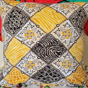 May include: A square patterned throw pillow with a patchwork design featuring yellow, black, and white geometric shapes and floral motifs.