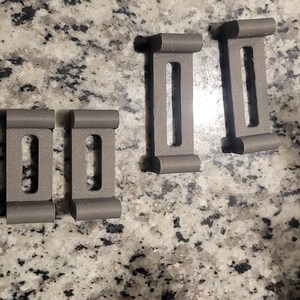 Puede incluir: Cuatro clips rectangulares de pl&aacute;stico gris con un agujero rectangular en el centro de cada clip.