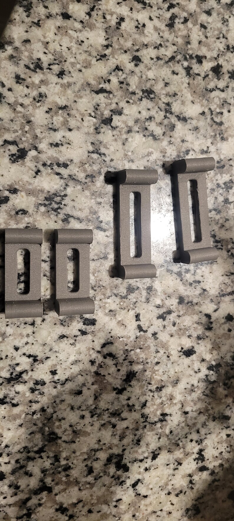 Puede incluir: Cuatro clips rectangulares de pl&aacute;stico gris con un agujero rectangular en el centro de cada clip.