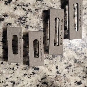 Puede incluir: Cuatro bloques de metal gris con el texto "CNC Gear -  #120141" impreso en cada bloque.