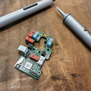 May include: A green circuit board with red and blue components, a silver screwdriver with the word "Wowstick" on it, and a silver solder sucker with the text "Viralloy Solder Sucker" on it.