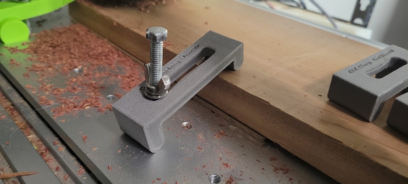 Puede incluir: Una abrazadera gris impresa en 3D con un tornillo roscado y una tuerca de metal. La abrazadera est&aacute; dise&ntilde;ada para sujetar la madera en su lugar mientras se trabaja en ella. La abrazadera est&aacute; sentada sobre una superficie de madera.