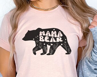 May include: A pink t-shirt with a black silhouette of a bear with the text "Mama Bear" in a retro font. The bear is surrounded by small floral and butterfly designs.