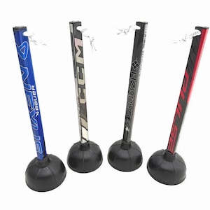 Op de afbeelding: Vier flessenstoppers in de vorm van hockeysticks met zwarte rubberen bases. De sticks zijn blauw, zwart en rood met witte veters. De sticks hebben de merknamen Bauer, CCM en HZRDUSE FX.