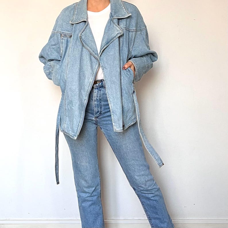 Puede incluir: Chaqueta vaquera azul claro con cintur&oacute;n envolvente y cremallera. La chaqueta se combina con vaqueros azul claro y una camiseta blanca. El conjunto es informal y elegante, perfecto para el d&iacute;a a d&iacute;a.