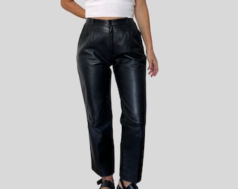 May include: Black leather pants with a high waist and straight leg. The pants have a classic design, with a button and zipper closure. The leather appears smooth and has a slight sheen. The pants are a versatile wardrobe staple.