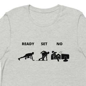 May include: A grey t-shirt with the words "Ready, Set, No" and a graphic of three stick figures in the stages of a race. The first figure is in the ready position, the second is in the set position, and the third is sitting in front of a computer.