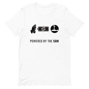 Può includere: Maglietta bianca con design grafico nero. La grafica presenta tre icone: mani giunte in preghiera, una batteria con un fulmine e una croce su una collina. Il testo "POWERED BY THE SON" è sotto le icone.