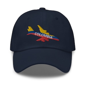 Könnte beinhalten: Eine marineblaue Baseballkappe mit einem gestickten Flugzeugdesign. Das Flugzeug ist in den Farben der kolumbianischen Flagge gefärbt: Gelb, Blau und Rot. Das Wort "COLOMBIA" ist in Weiß auf das Flugzeug gestickt.