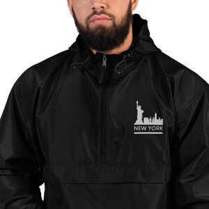May include: Black hooded anorak jacket with a half-zip closure. The jacket features a white graphic of the New York City skyline, including the Statue of Liberty, with the text "NEW YORK" below it.