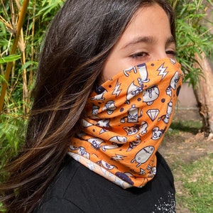 Op de afbeelding: Een jong persoon draagt ​​een feloranje gezichtsmasker met een wit en zwart cartoonpatroon. Het masker is gemaakt van een zachte, ademende stof en heeft een verscheidenheid aan leuke en fantasierijke personages.