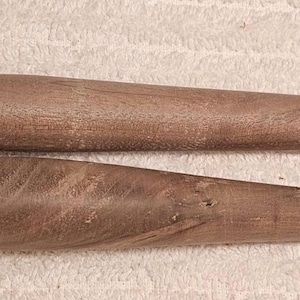 May include: Two wooden yarn swift sticks, each with a pointed end and a rounded end. The sticks are a medium brown color and appear to be handmade. The sticks are lying parallel to each other.