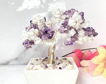 Könnte beinhalten: Ein weißer Keramiktopf mit einer Drahtskulptur eines Baumes aus weißen und violetten Steinen. Der Baum steht in einem weißen Keramiktopf vor einem weißen Hintergrund.