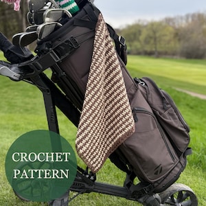 May include: A brown and cream crochet golf towel hangs from a golf bag on a golf cart. The towel has a striped pattern and a brown border. The golf bag is brown and black, and the cart is black. The text "CROCHET PATTERN" is in a green circle.