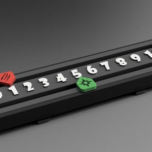 May include: A black rectangular game board with white numbers 0 through 10. A red marker with a star symbol is on the number 0. A green marker with a star symbol is on the number 6.