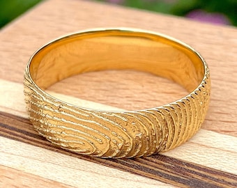 May include: A gold band ring with a textured fingerprint design.