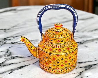 May include: A yellow teapot with a blue handle and intricate floral patterns in red and black. The teapot has a spout and a lid with a red and yellow design. The handle is blue with white stripes. The teapot is sitting on a marble surface.