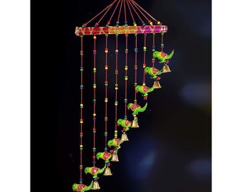 May include: A decorative hanging mobile featuring green parrot figures with golden bells. The mobile has a colorful, beaded top and red string accents. The parrots are arranged in a descending pattern, creating a visually appealing design.