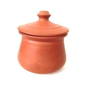 May include: A terracotta-colored ceramic jar with a lid. The jar has a rounded body and a lid with a small knob on top. The jar and lid are a uniform reddish-brown color, suggesting a natural clay material.