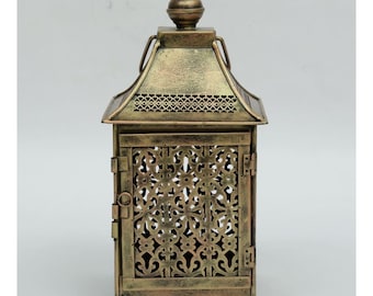Puede incluir: Una linterna decorativa de estilo antiguo con un acabado dorado envejecido. La linterna de metal presenta intrincados patrones calados en los laterales y una puerta con bisagras. Tiene un techo puntiagudo y un pequeño remate en la parte superior.