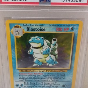May include: A PSA graded Blastoise Pokemon card from the 1999 Pokemon Game set. The card is a holographic card and is in near mint condition. The card features a blue Blastoise with a large cannon on its back. The card is graded NM-MT 8.