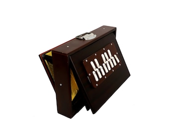 May include: A brown wooden harmonium with a closed lid and a row of white keys visible. The harmonium is folded up and ready to be carried.