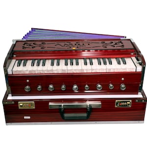 May include: A red harmonium with a keyboard, bellows, and a carrying case. The harmonium has a decorative floral design on the top and the text "AMRIT SINCE 1971".