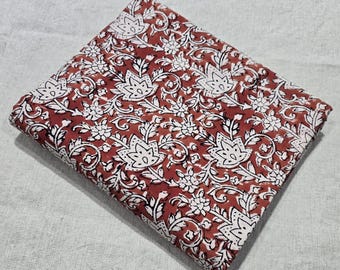 May include: Folded square of fabric with a repeating floral pattern in white and rust-red. The design features stylized flowers and leaves, creating a detailed and ornate textile. The fabric appears to be cotton or a similar natural fiber.