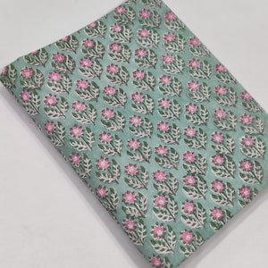 May include: A folded piece of fabric with a repeating floral pattern. The design features pink flowers with white and green leaves on a light teal background. The fabric appears to be cotton or a similar material, suitable for sewing or crafting projects.